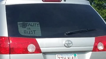 A car with a sign in the back window "Totality or bust."
