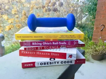 Another pile of diet and fitness books and a dumbbell.